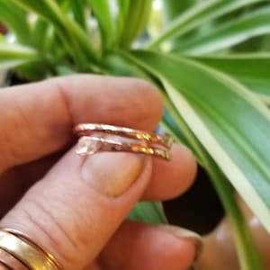 May include: Two hammered copper rings stacked on a finger. The rings are a warm, reddish-brown color and have a textured surface.