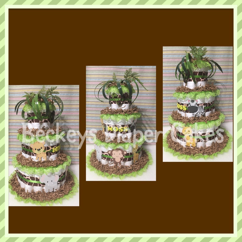 Op de afbeelding: Een drielaagse luiercake versierd met jungledieren thema's. De cake is ingepakt in bruin en wit gestreept stof en groen en wit gerimpeld stof. De bovenste laag heeft een groene plant, de middelste laag heeft het woord "Moss" in bruine letters, en de onderste laag heeft een bruine olifant, een bruine aap en een bruine leeuw.