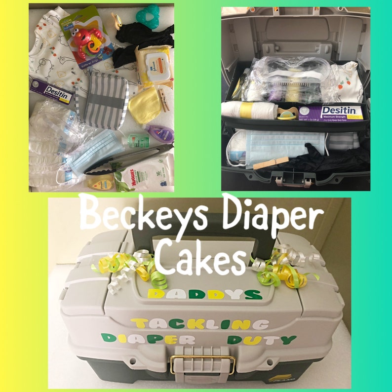 May include: A grey tackle box with the words "Daddy's Tackling Diaper Duty" on the front. The box is decorated with yellow and green ribbons and is filled with baby supplies, including nappies, wipes, and a dummy.