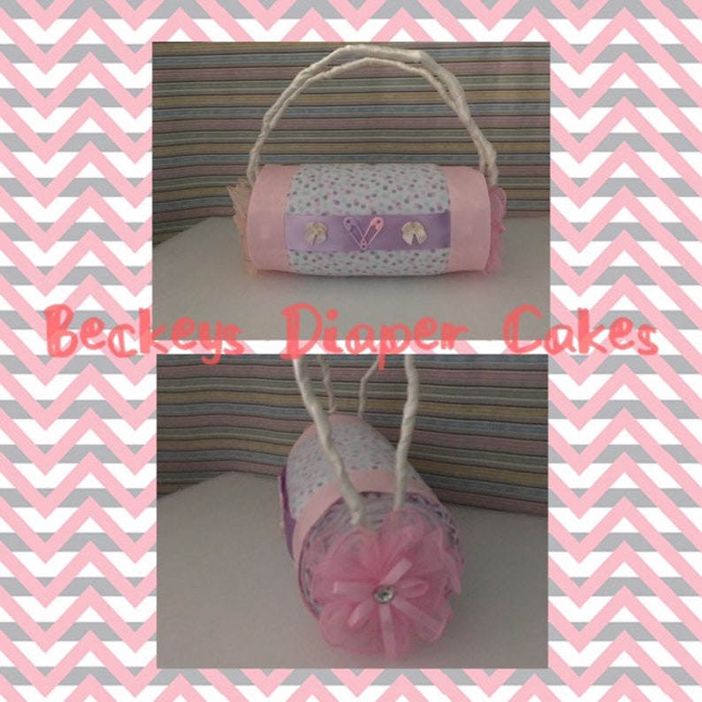 May include: A pink and purple diaper cake with a white handle and a pink bow. The cake is decorated with white polka dots and a purple ribbon. The text "Beckeys Diaper Cakes" is visible in the image.