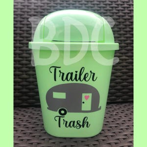 以下が含まれることがあります： トレーラーのシルエットと「Trailer Trash」というテキストが書かれた明るい緑色のゴミ箱です。