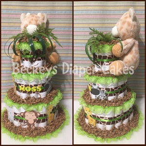 Op de afbeelding: Een drielaagse luiercake versierd met een giraffen-, zebra- en apenprint. De cake is versierd met groene en bruine papieren strooisel en groene kant. De bovenste laag heeft een knuffelgiraf erop. De middelste laag heeft een bruin lint met de naam "Moss" erop.