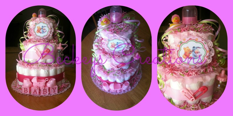 May include: A three-tiered diaper cake decorated with pink and green ribbons, bows, and flowers. The cake features Winnie the Pooh and Tigger characters, along with the words "Baby" on the bottom tier.