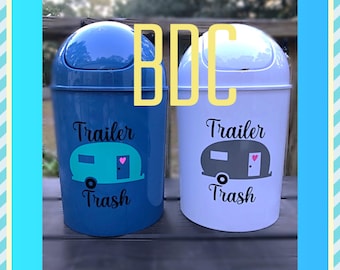 May include: Two small trash cans with lids, one blue and one white, with a camper trailer graphic and the text "Trailer Trash" on each.