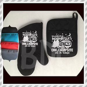 May include: A black oven mitt and pot holder set with the text "making memories ONE CAMPSITE at a time" in white. The design includes a camper, trees, and a crescent moon. A multi-colored pot holder is on the left.