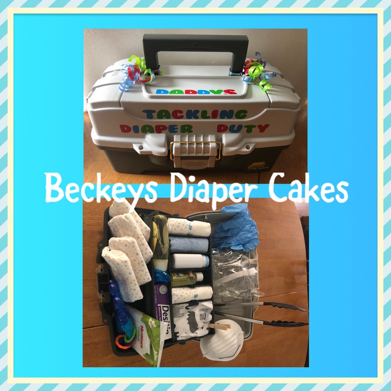 May include: A white tackle box with the text "Daddy's Tackling Diaper Duty" on the lid. The box is open and filled with baby supplies, including nappies, wipes, lotion, and a dummy.
