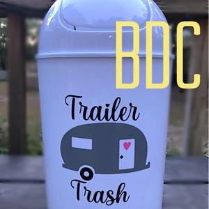 以下が含まれることがあります： 白のプラスチック製のゴミ箱に、黒とグレーのキャンピングカーのデザインと「Trailer Trash」の文字が書かれています。