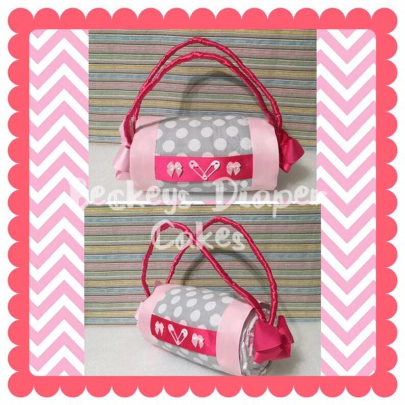 May include: A grey and white polka dot diaper cake with pink ribbon and safety pins. The cake is shaped like a handbag with a pink handle.