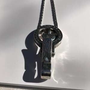 May include: A silver necklace with a heart-shaped pendant and a circular charm with intricate designs. The charm has a small heart in the center.