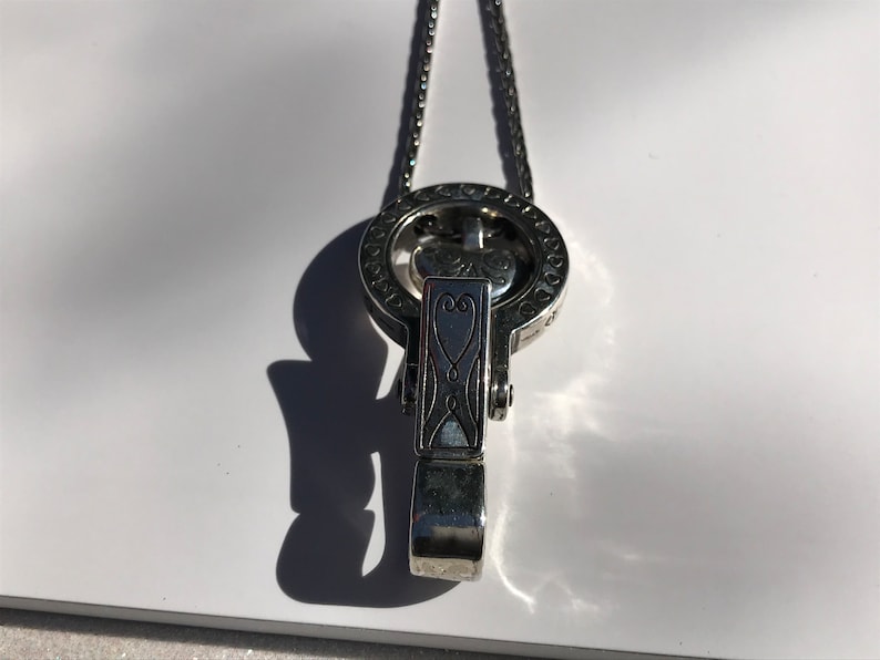 May include: A silver necklace with a heart-shaped pendant and a circular charm with intricate designs. The charm has a small heart in the center.