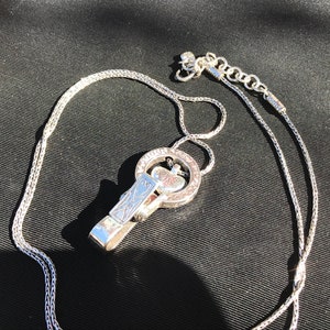 May include: A silver chain necklace with a silver pendant featuring a heart design. The pendant is attached to a silver clip.