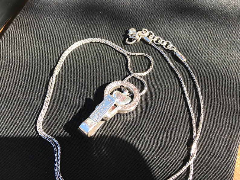 May include: A silver chain necklace with a silver pendant featuring a heart design. The pendant is attached to a silver clip.