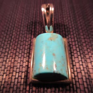 Peut inclure: Un pendentif en turquoise avec un sertissage en argent. La pierre est de forme rectangulaire et a une surface lisse et polie.