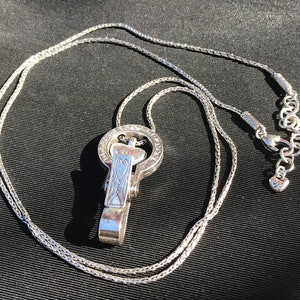 May include: A silver chain necklace with a silver pendant featuring a heart design and intricate details. The pendant has a clasp that can be used to attach other charms or accessories.