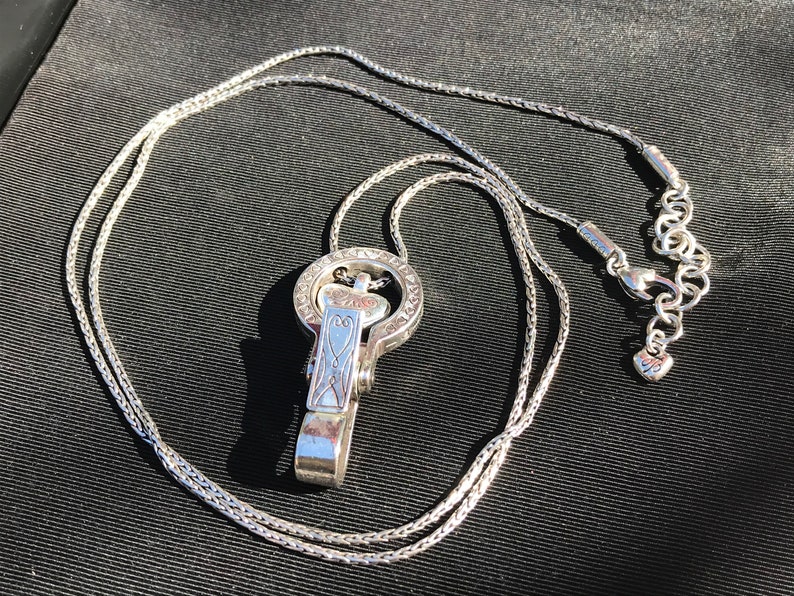 May include: A silver chain necklace with a silver pendant featuring a heart design and intricate details. The pendant has a clasp that can be used to attach other charms or accessories.