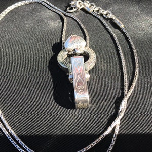 May include: A silver chain necklace with a heart-shaped pendant and a decorative clasp. The pendant and clasp feature intricate engraved designs.