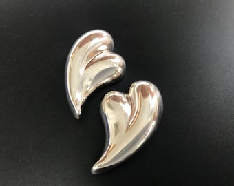 May include: A pair of silver heart-shaped earrings. The earrings are smooth and shiny.