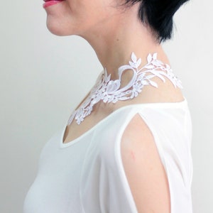 Puede incluir: Un collar gargantilla de encaje blanco con un dise&ntilde;o floral. El collar lo lleva una persona con el pelo negro corto.
