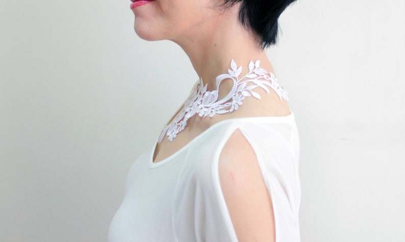 Puede incluir: Un collar gargantilla de encaje blanco con un dise&ntilde;o floral. El collar lo lleva una persona con el pelo negro corto.