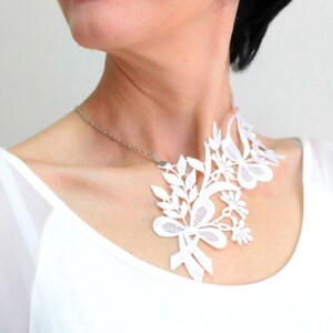 Puede incluir: Un collar de encaje blanco con un dise&ntilde;o floral. El collar lo lleva una persona con el pelo negro corto.