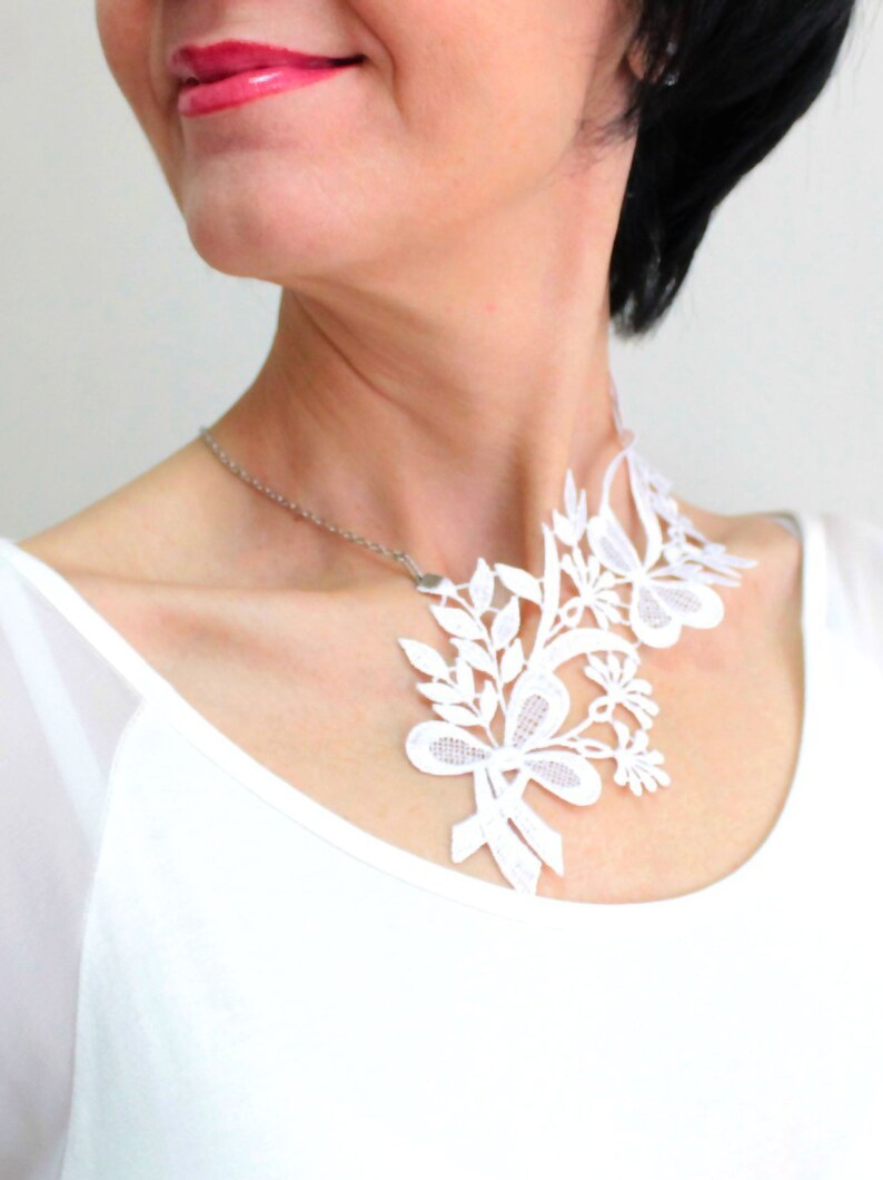 Puede incluir: Un collar de encaje blanco con un dise&ntilde;o floral. El collar lo lleva una persona con el pelo negro corto.