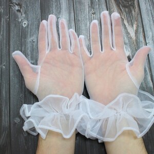 May include: A pair of white lace gloves with ruffled cuffs. The gloves are sheer and delicate, and the cuffs are made of a soft, flowing fabric.