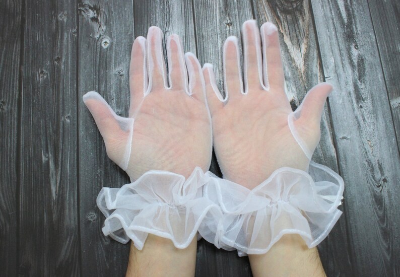 May include: A pair of white lace gloves with ruffled cuffs. The gloves are sheer and delicate, and the cuffs are made of a soft, flowing fabric.