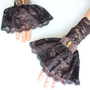 May include: A pair of brown lace wrist cuffs with a ruffled edge and a small jeweled embellishment.