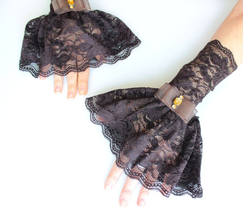 May include: A pair of brown lace wrist cuffs with a ruffled edge and a small jeweled embellishment.