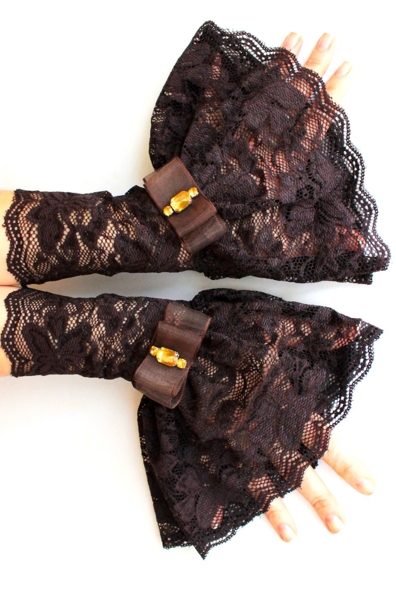 May include: A pair of brown lace gloves with a ruffled cuff and a jeweled bow accent.