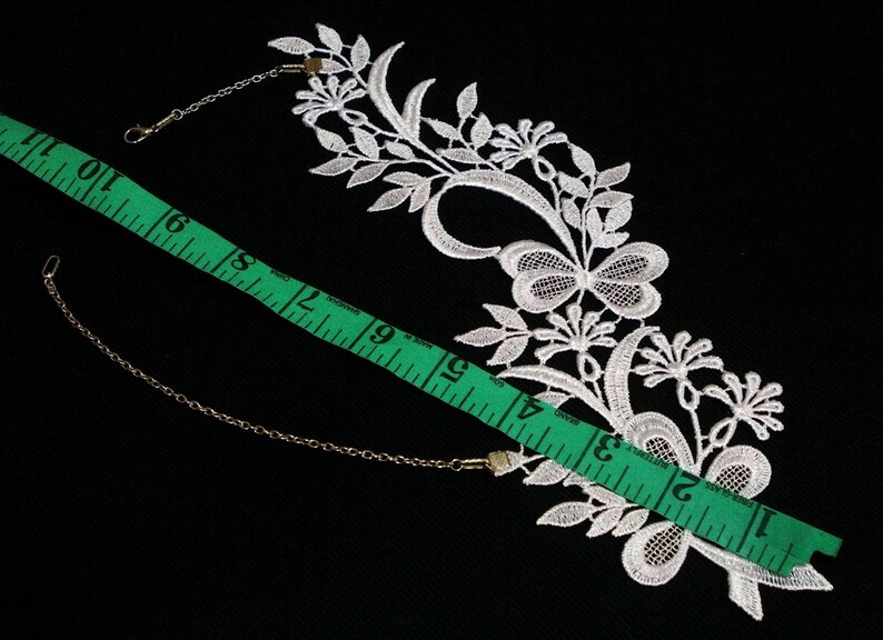 Puede incluir: Borde de encaje blanco con un dise&ntilde;o de mariposa y detalles florales. El borde mide aproximadamente 15 pulgadas de largo e incluye dos conectores de cadena de metal.
