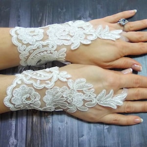 Könnte beinhalten: Ein Paar weiße fingerlose Handschuhe aus Spitze mit Blumenstickerei. Die Handschuhe sind aus zartem, durchsichtigem Stoff gefertigt und haben einen zarten, femininen Look.