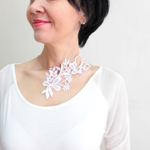 Puede incluir: Un collar gargantilla de encaje blanco con un dise&ntilde;o floral. El collar es delicado e intrincado, con una variedad de formas de flores y hojas.