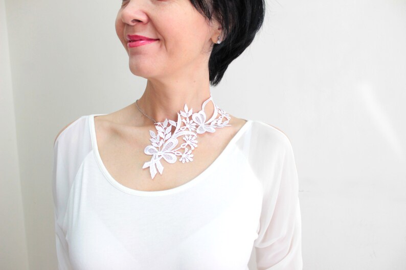Puede incluir: Un collar gargantilla de encaje blanco con un dise&ntilde;o floral. El collar es delicado e intrincado, con una variedad de formas de flores y hojas.