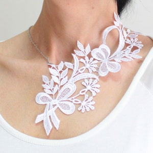 Puede incluir: Un collar gargantilla de encaje blanco con un dise&ntilde;o floral. El collar es delicado e intrincado, con un lazo en el centro.