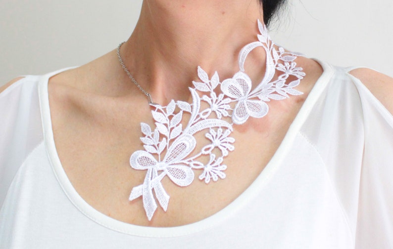 Puede incluir: Un collar gargantilla de encaje blanco con un dise&ntilde;o floral. El collar es delicado e intrincado, con un lazo en el centro.