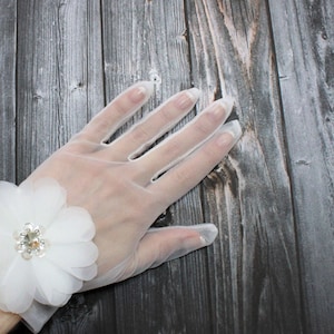 May include: White sheer gloves with a white flower embellishment on the wrist. The flower has a rhinestone center.