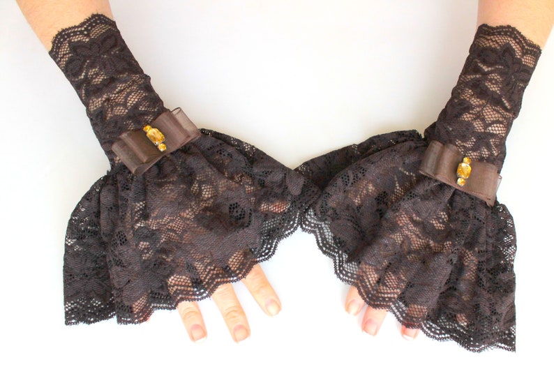 May include: A pair of brown lace wrist cuffs with a brown satin bow and a gold-toned embellishment on each cuff.