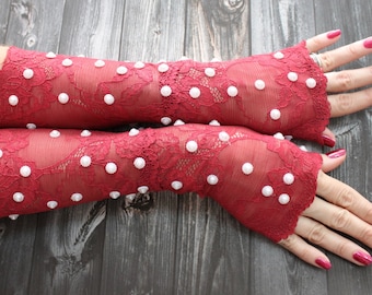 May include: A pair of red lace fingerless gloves with white pearl embellishments.
