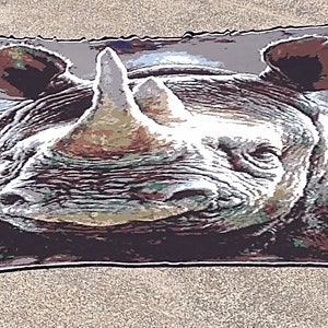 May include: Close-up of a black and white rhinoceros face on a gray and brown patterned throw blanket.