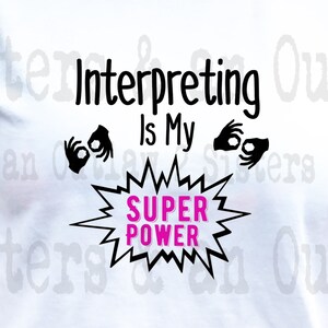 May include: White t-shirt with black text that reads "Interpreting is my Super Power" with two black hand signs on either side of the text. The text "Super Power" is in a pink speech bubble.