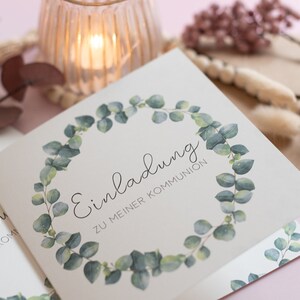 Puede incluir: Una tarjeta blanca con una corona de eucalipto verde alrededor del texto "Einladung zu meiner Kommunion".