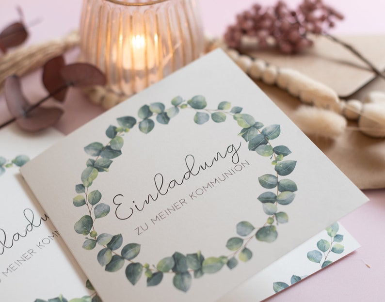 Puede incluir: Una tarjeta blanca con una corona de eucalipto verde alrededor del texto "Einladung zu meiner Kommunion".