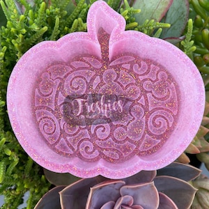 May include: Pink glitter resin pumpkin dish with a swirl design. The dish is shaped like a pumpkin and has a raised stem.