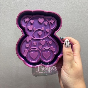 May include: A purple and pink teddy bear-shaped mold with heart details. The mold has a layered design, with a darker purple outline and a lighter purple interior. The text "Freshies" is visible in the image.