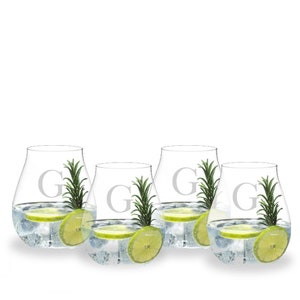 May include: Four clear stemless glasses filled with ice, a lime slice, and a sprig of rosemary. Each glass has the letter "G" etched on the front. The glasses are set against a white background, suggesting a refreshing beverage.