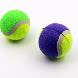 May include: Two tennis balls, one green and one purple, with a white seam. The balls are made of a soft, fuzzy material.