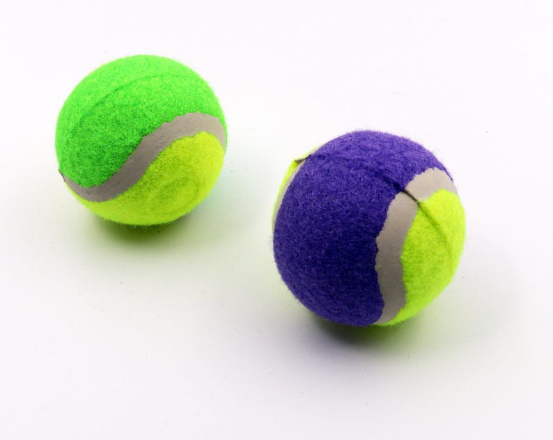 May include: Two tennis balls, one green and one purple, with a white seam. The balls are made of a soft, fuzzy material.