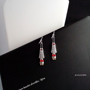 Peut inclure: Boucles d'oreilles pendantes argentées et rouges avec un design géométrique. Les boucles d'oreilles sont sur un fond noir avec le texte "Bijoux createurs boucles d'oreilles. Néra" et "Jewelry by El666".