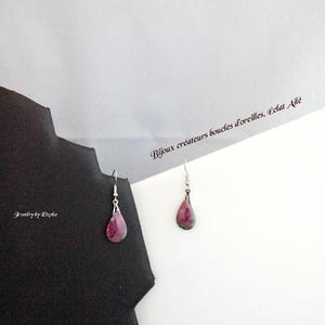 Könnte beinhalten: Ein Paar tropfenförmige Ohrringe mit einem silbernen Haken. Die Ohrringe haben einen leuchtend rosa-grünen Edelstein. Der Hintergrund enthält den Text "Bijoux créateurs boucles d'oreilles. Éclat Ailé" und "jewelry by Eliza".